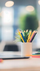Assorted colored pencils and green sprouts sit neatly inside a white ceramic pot on a table