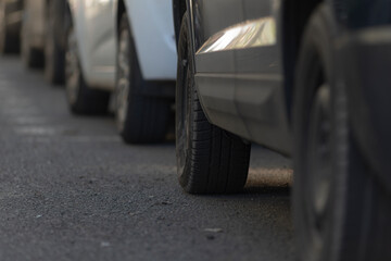 car wheel details, urban residential scene with focused wheels near curb and textured pavement, close examination of vehicle tires aligned by curb emphasizing urban parking conditions and surface © Viktar