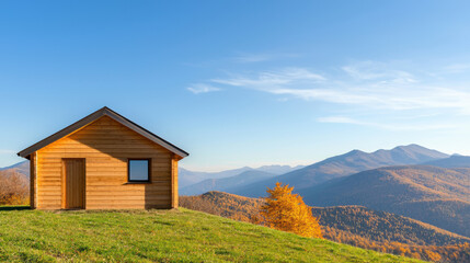  wooden cabin sits on a green hillside, overlooking a scenic view of mountains and autumn foliage under a clear blue sky.