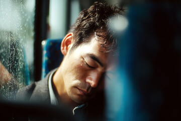 Tired adult man sleeping on public transportation, showing physical exhaustion and mental fatigue during daily urban commuting.