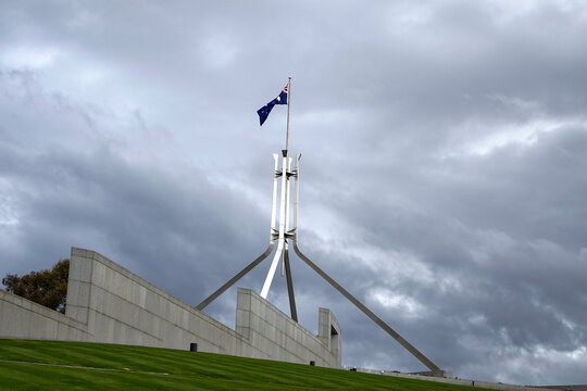 The Australian National Flag Flying High Above Parliament House in Canberra on a Cloudy Overcast Day.