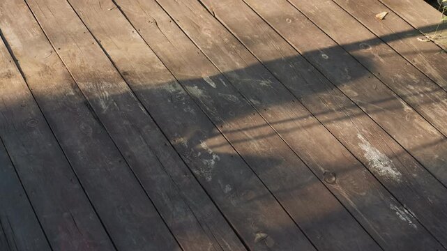 Long Shadow Crossing Sunlit Wooden Deck, Strong Horizontal Stripe From Fence Silhouette, Textured Planks And Evening Glow, Dramatic Contrast And Slow Shifting Light, Moody Outdoor Scene