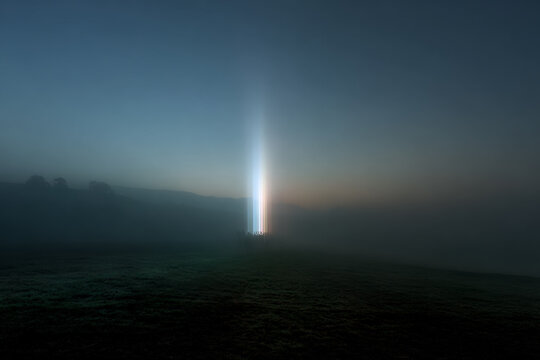 A vertical beam of blue light piercing through dense fog in a dark mountain landscape under the night sky.