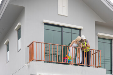 Experienced bearded foreman shows new home plans on a tablet to a smiling mother and daughter over terrace, highlighting smart construction technology and a warm, hopeful future in their house