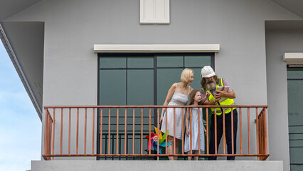 Experienced bearded foreman shows new home plans on a tablet to a smiling mother and daughter over terrace, highlighting smart construction technology and a warm, hopeful future in their house