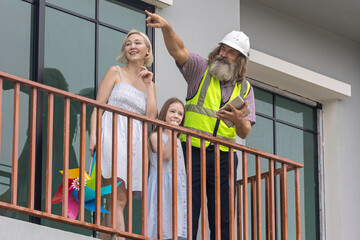 Experienced bearded foreman shows new home plans on a tablet to a smiling mother and daughter over terrace, highlighting smart construction technology and a warm, hopeful future in their house