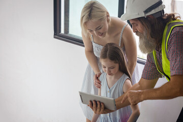 Experienced bearded foreman shows new home plans on a tablet to a smiling mother and daughter, highlighting family trust, smart construction technology and a warm, hopeful future in their house