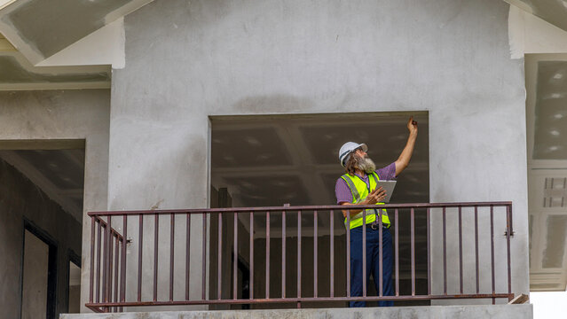 Experienced bearded construction foreman uses a digital tablet inside a new house, checking plans and managing the modern building project with confidence, precision and smart technology