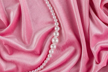 Beautiful festive background of velvet pink fabric with white pearl beads. Chic string of pearls among delicate folds of fabric material. top view.