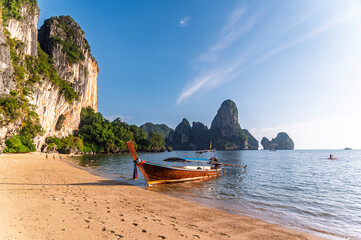 Traditional Thai longtail boat anchored on a peaceful tropical beach with  Railay Beach and high limestone cliffs background, Ao Nang, Krabi, Thailand