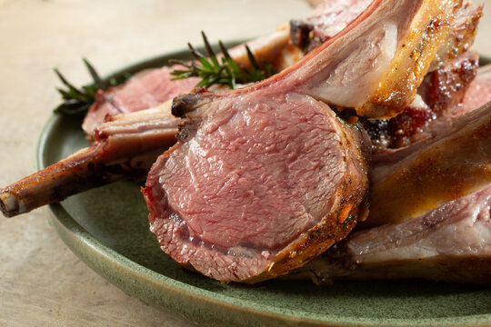 A view of a pile of medium rare lamb rack slices, on a plate.