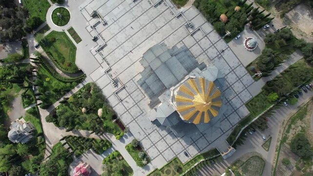 Aerial drone view over the Holy Trinity Cathedral (Sameba) in Tbilisi, Georgia, featuring the iconic golden dome and surrounding cityscape. High-quality 4K footage.