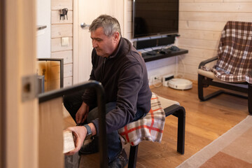 Senior man loading firewood into home fireplace indoors 