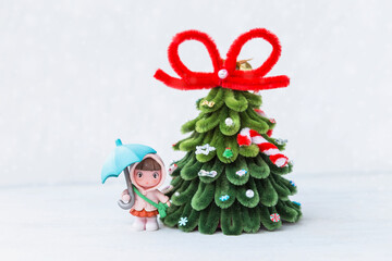Christmas tree with miniature girl in raincoat holding blue umbrella on white background, Christmas card background idea