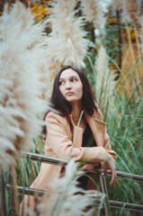 A beautiful young woman with dark hair, holding a smartphone, stands among fluffy autumn plants. Vertical photograph.
