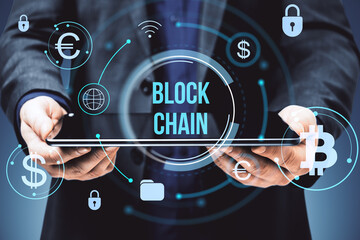 Businessman holding tablet with blockchain and cryptocurrency icons on virtual screen in digital financial network interface concept on dark background.