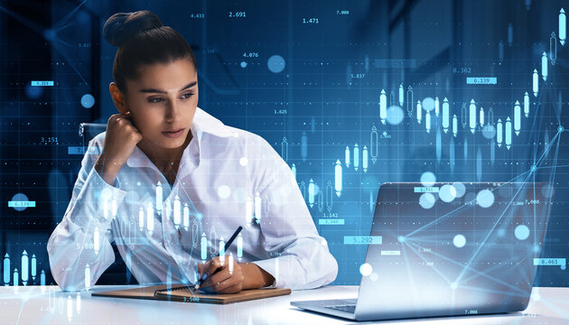 Businesswoman analyzing financial data at desk with laptop and digital charts in modern office background, representing investment and stock growth.