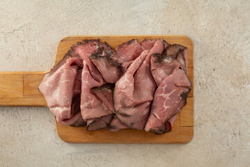 A top down view of a wood board of roast beef deli slices.