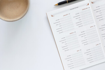 Financial planning concept with monthly budget planner notebook, pen, and coffee cup on white desk. Top view personal finance management and investment goals for saving money and wealth success.