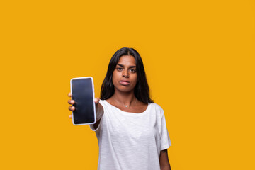 Naklejka premium Young woman showing smartphone screen on yellow background