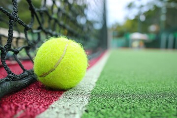 Tennis ball rests against net on textured court surface closeup