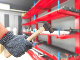 Worker hand holding rustic hammer over working rooom or warehouse background in factory..
