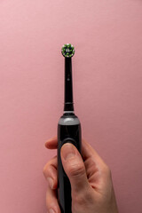 Electric toothbrush in female hand on pink background