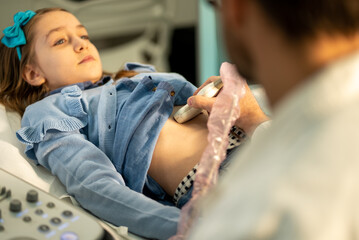 Doctor performs ultrasound scan on a young girl's abdomen in a medical examination room