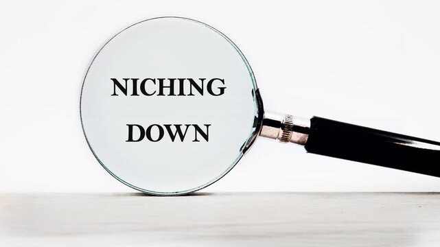 A magnifying glass zooms in to clarify the message NICHING DOWN. An artistic representation of focusing your business for success in the marketplace