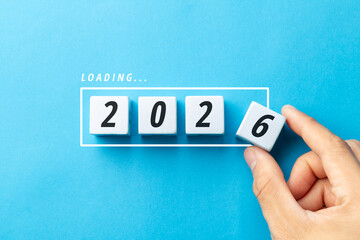 Hand completing the year 2026 by placing the final white number block on a blue background. Minimalist concept of achievement, goal setting, and strategic preparation for the future.