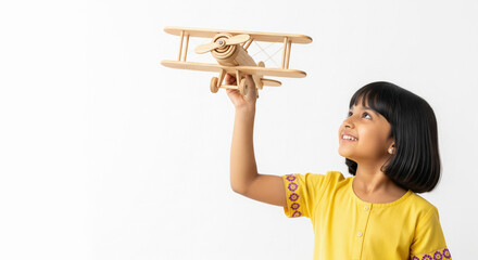 Young Indian girl in a yellow kurta playfully holding up a wooden toy airplane against a clean white studio background,