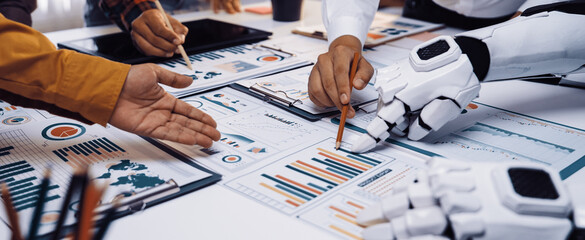 In a modern workspace, human and robotic hands collaborate to analyze data charts, showcasing the blend of technology and teamwork in a business meeting setting.Noogenesis