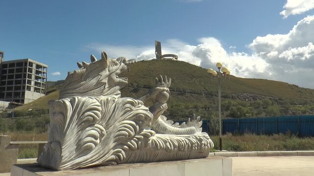 MONGOLIA, ULAANBAATAR - August 30, 2013: Buddha Park. A dragon figure guarding a standing Buddha on a sunny summer day, with the mountain and the Zaisan memorial complex in the background.