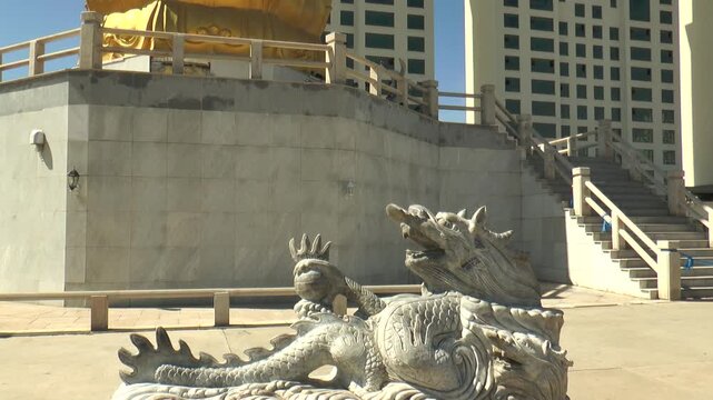 MONGOLIA, ULAANBAATAR - August 30, 2013: Buddha Park. A dragon figure guarding a standing Buddha on a sunny summer day, with the mountain and the Zaisan memorial complex in the background.
  