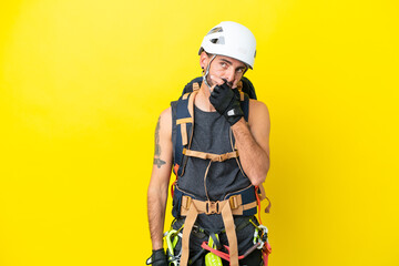 Young caucasian rock climber man isolated on yellow background having doubts and with confuse face expression