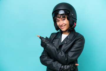 Young Argentinian woman with a motorcycle helmet isolated on blue background pointing finger to the side