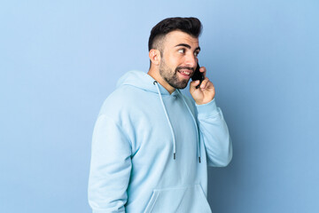 Caucasian man over isolated blue background keeping a conversation with the mobile phone with someone