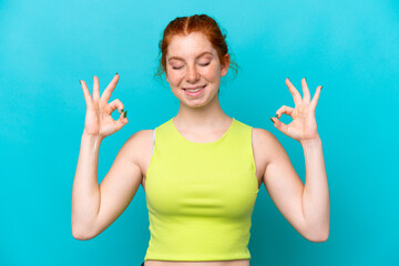 Fototapeta premium Young reddish woman isolated on blue background in zen pose