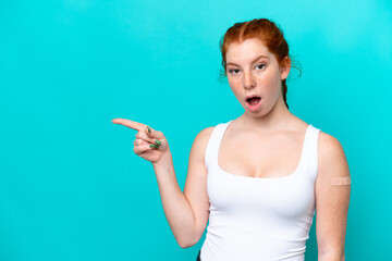 Fototapeta premium Young reddish woman wearing a band aids on blue background surprised and pointing side