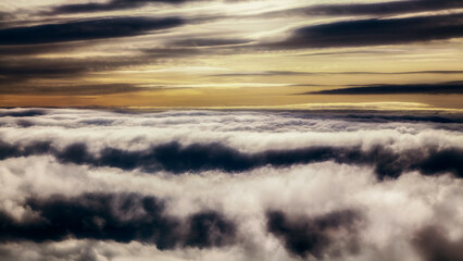Dramatic layered clouds forming atmospheric cloud inversion above landscape at sunrise