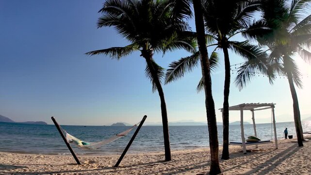 Golden sands stretch along the serene shoreline of Koh Phayam Thailand, where tall palm trees dance in the gentle breeze. Guests relax in hammocks while waves softly lap at the beach.