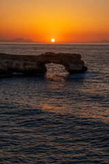 Sunset behind the Arch of Skaleta natural sea arch with glowing orange sky and calm Mediterranean Sea