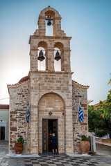 Stone church with bell tower in Panormos village on Crete featuring traditional architecture and Greek flags