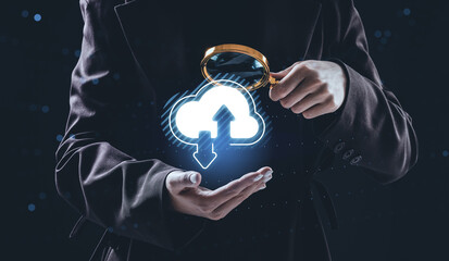 Businessperson examining glowing cloud upload and download hologram with magnifying glass, symbolizing online data storage and internet technology concept.