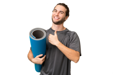 Young sport man going to yoga classes while holding a mat over isolated background giving a thumbs up gesture