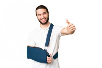 Young handsome man with broken arm and wearing a sling over isolated chroma key background giving a thumbs up gesture