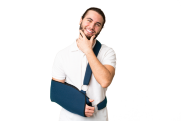 Young handsome man with broken arm and wearing a sling over isolated chroma key background happy and smiling