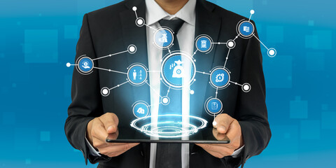 A businessman in a suit holds a tablet showcasing digital connections and icons, symbolizing technology and innovation in a corporate setting. The blue background accentuates the modern theme. Tessel
