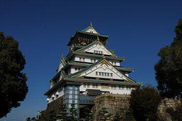 Naklejka premium The Osaka-jo Castle Tower in Japan, with White Walls and a Green Roof, Against a Clear Blue Sky
