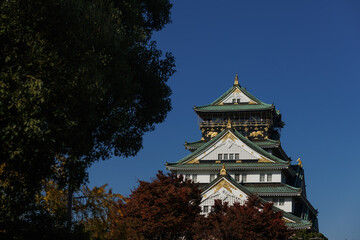 Fototapeta premium The Osaka-jo Castle Tower in Japan, with White Walls and a Green Roof, Against a Clear Blue Sky